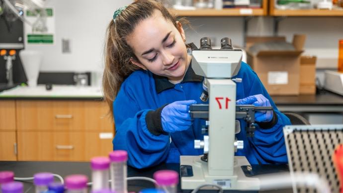 Anna Gonzalez, in a blue lab coat, adjusts a sample under a microscope