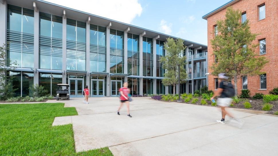 Outside view of Dicke Hall's glass wall with students walking by