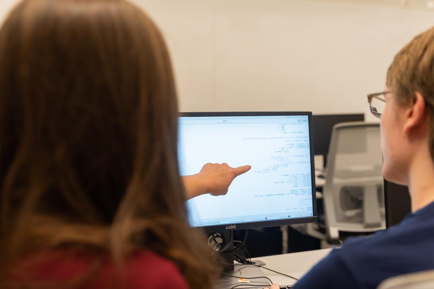 一个学生指着电脑屏幕，另一个学生看着