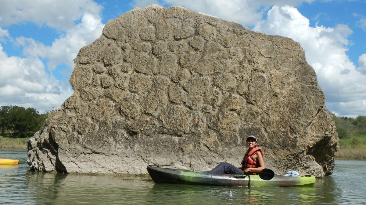 person on a kayak in the river with a big rock as the back landscape