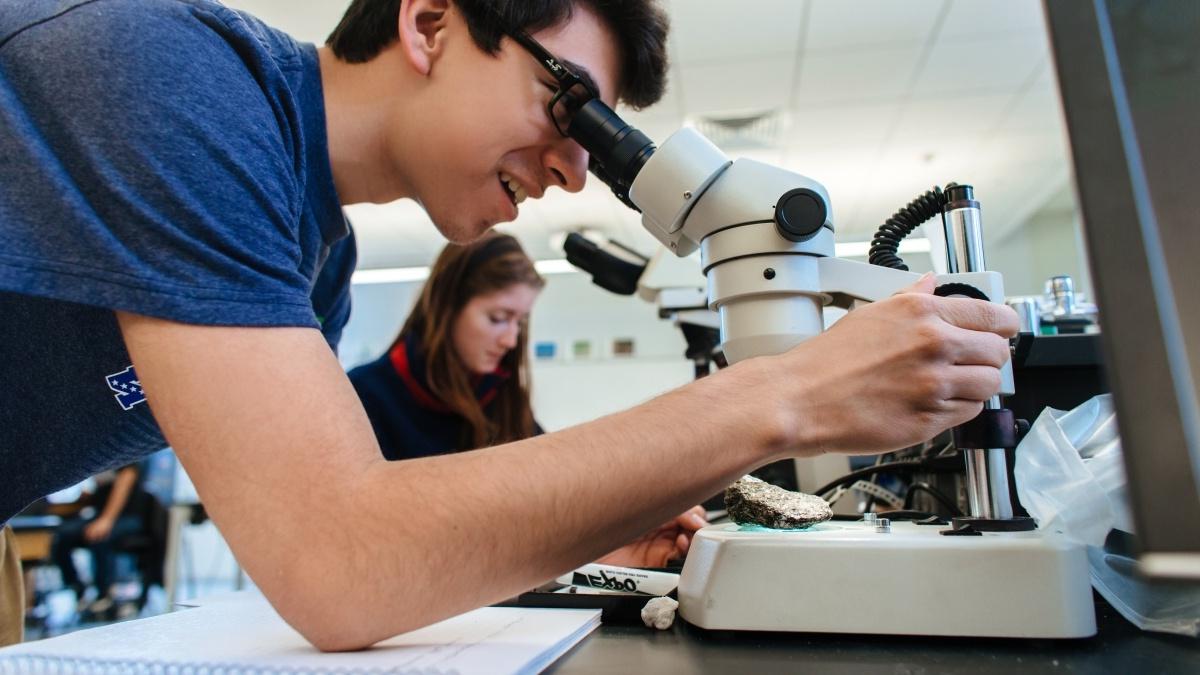 Student looking into a microscope with another student in the background