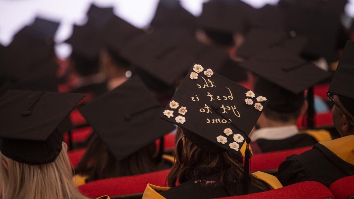 一名学生在毕业典礼上戴着一顶设计有鲜花和“最好的还在后头”字样的毕业帽.
